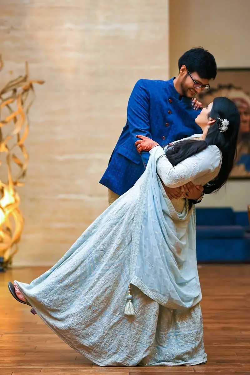 A groom in a blue bandhgala dipping the bride backwards, her ice-blue lehenga and dupatta sweeping the floor.